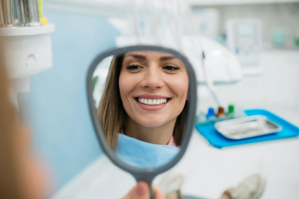 Patient smiling while checking teeth in the mirror after teeth whitening treatment in Pittsburgh, PA